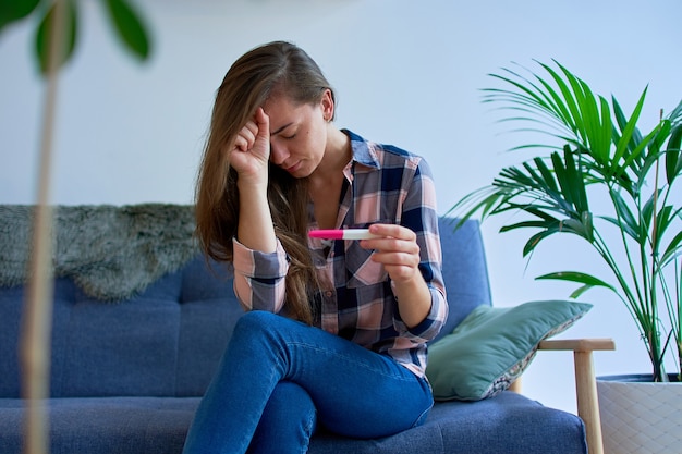 Una mujer de ansiedad llorando deprimida molesta triste sentada sola y sosteniendo la prueba de embarazo