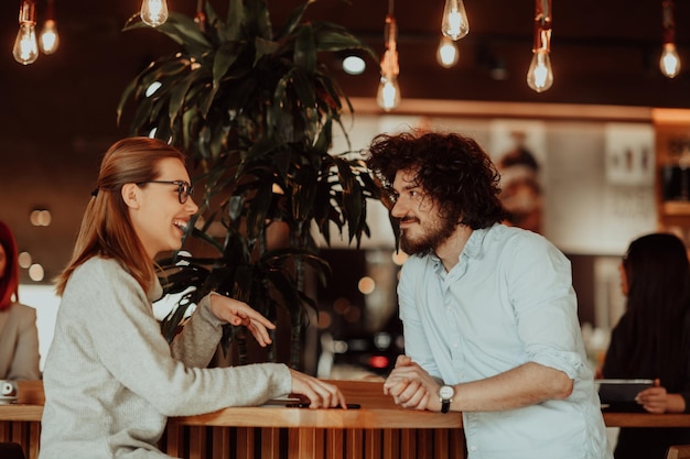 una mujer con anteojos y un hombre con cabello afro se sientan en un café y hablan sobre proyectos de negocios