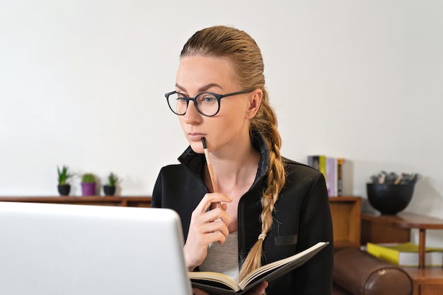 Mujer con anteojos y portátil estudiando trabajando en línea de forma remota