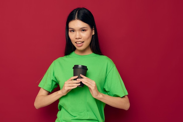 Mujer con apariencia asiática en una camiseta verde un vaso de bebida divertido fondo aislado inalterado