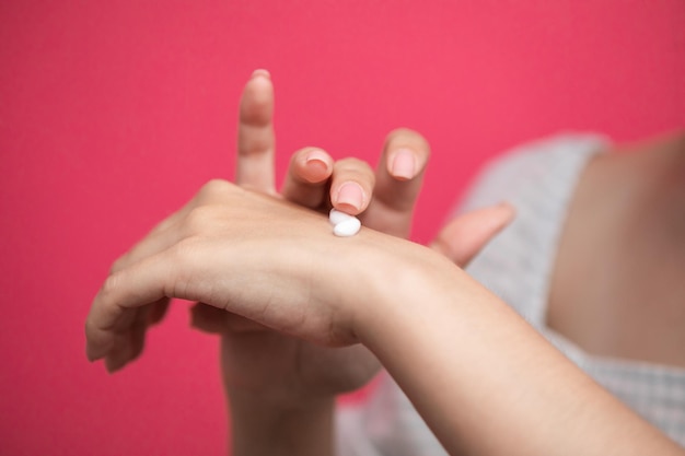 Mujer aplica crema en sus manos aislado sobre fondo de color rosa