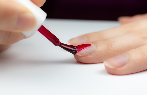 Foto la mujer aplica esmalte de uñas rojo. chica haciendo una manicura. procedimientos de salón a domicilio. hermosas manos y uñas. de cerca, foto macro.