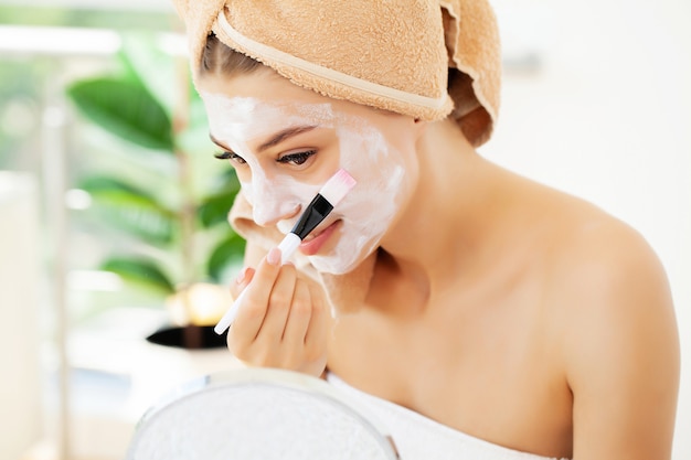 Foto mujer aplica mascarilla de arcilla blanca para el cuidado de la piel facial en el baño de lujo del hotel