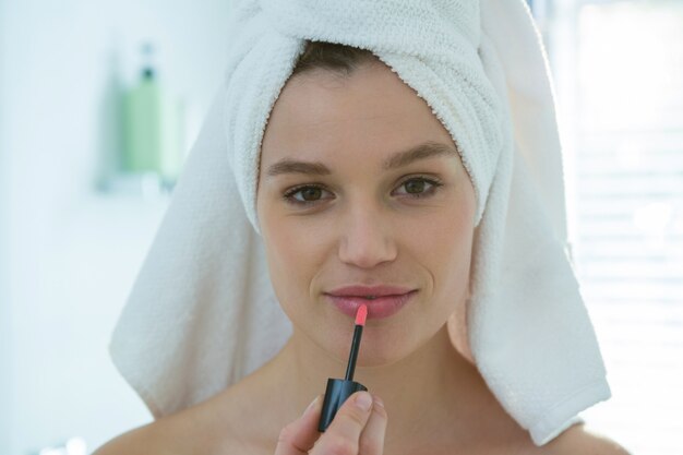 Mujer aplicando brillo labial en sus labios en el baño.