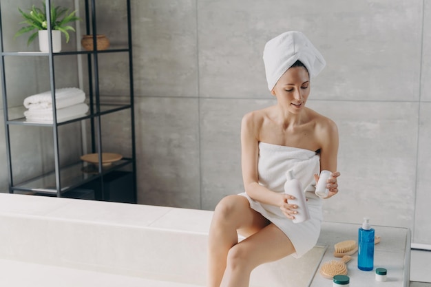 Mujer aplicando cosméticos hidratantes para el cuidado de la piel del cuerpo después de ducharse en el baño