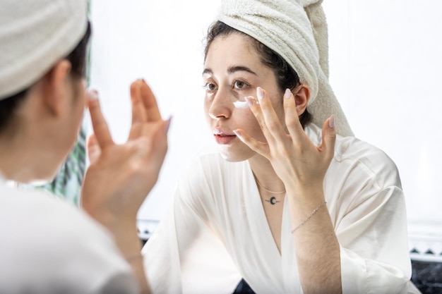 Mujer aplicando crema en la cara frente al espejo del baño