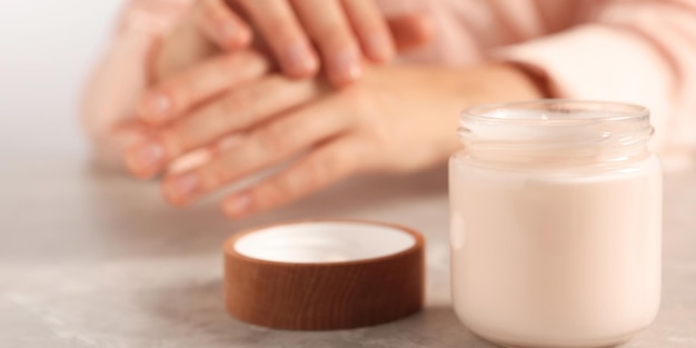 Mujer aplicando crema cosmética en la mano en la mesa gris centrada en el diseño de la pancarta del tarro