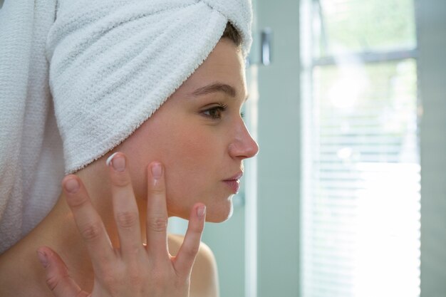 Mujer aplicando crema hidratante en la cara en el baño.