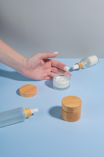 Mujer aplicando crema en la mano sobre fondo azul con productos cosméticos y sombras duras Concepto de tratamiento para el cuidado de la piel