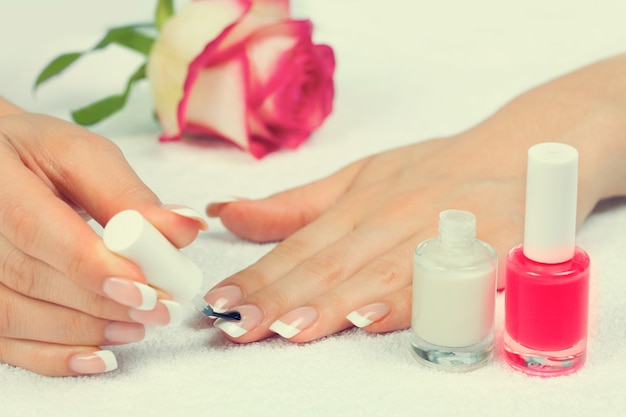 Mujer aplicando esmalte de uñas para una manicura francesa perfecta en una toalla blanca