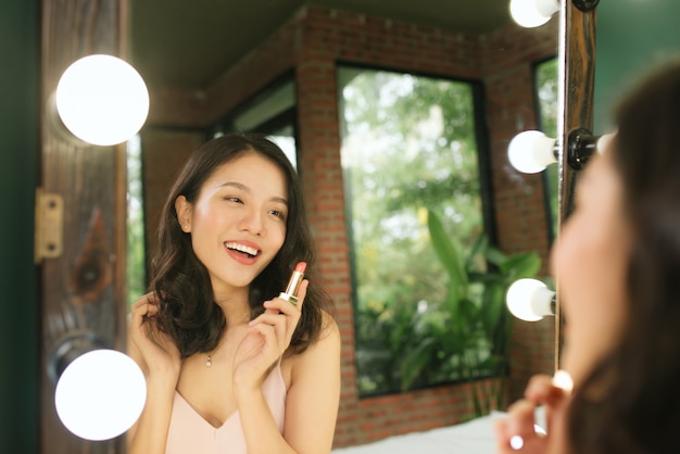 Mujer aplicando lápiz labial mirando en el espejo. Hermosa chica hace maquillaje