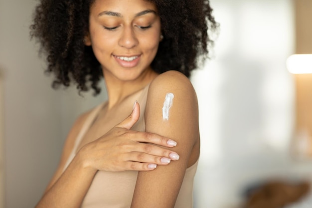 Foto mujer aplicando loción o crema hidratante sobre sus hombros, cuidando su piel en casa, de pie