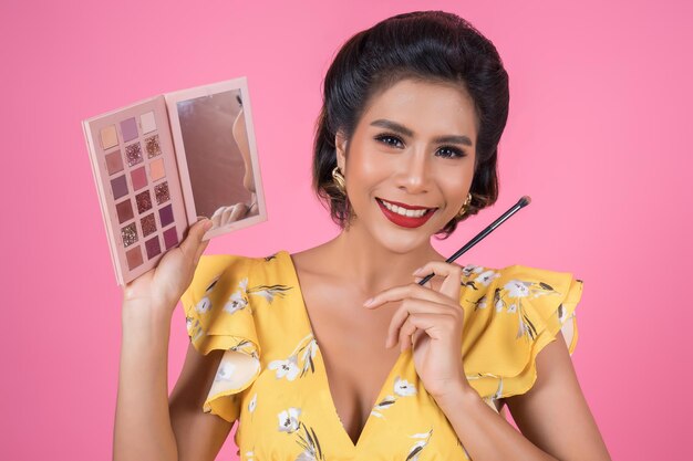 Foto mujer aplicando maquillaje contra un fondo rosado