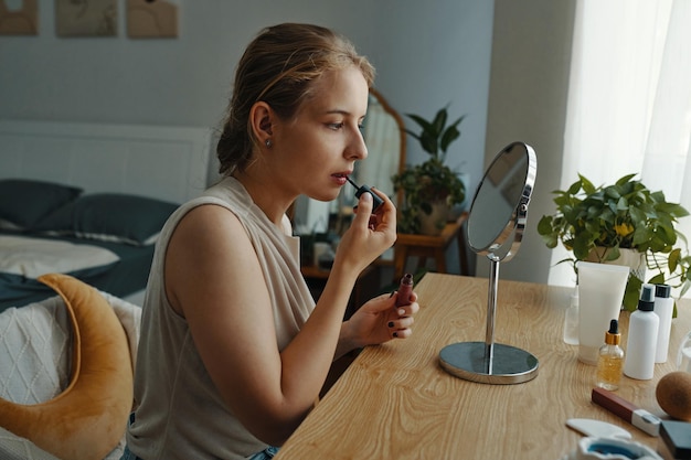 Mujer aplicando maquillaje en un entorno de dormitorio moderno