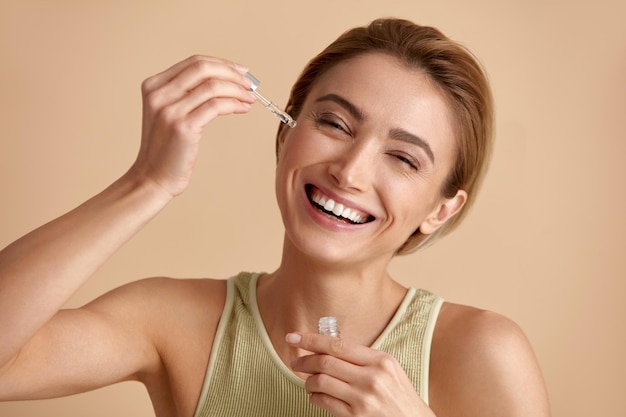 Mujer aplicando suero en la cara Mujer aplicando aceite esencial en la piel de la cara