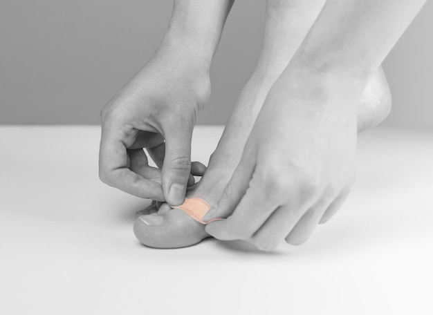 Mujer aplicando yeso médico en el dedo del pie Concepto de medicina de primeros auxilios Corta abrasiones y sangra ligeramente heridas callos curación Blanco y negro