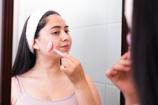 Una mujer aplicándose una mascarilla rosa frente a un espejo.