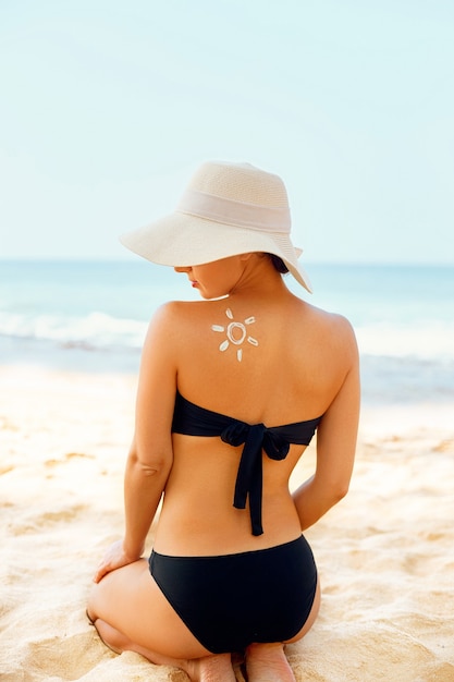 Mujer aplicar crema solar en el hombro bronceado en forma de sol.