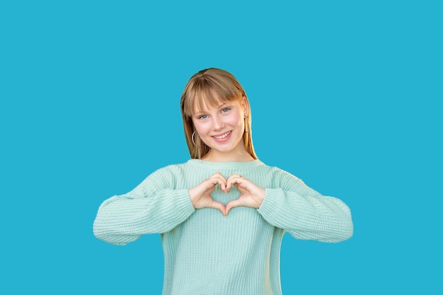 Mujer de apoyo Mensaje romántico Amor cuidado Admiración afecto Retrato de feliz dama alegre en suéter mostrando gesto de corazón sonriendo aislado sobre fondo de espacio de copia azul