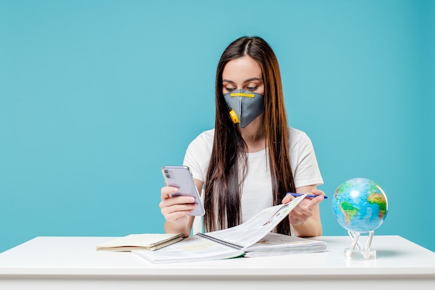 Mujer aprendiendo con el planeta tierra y teléfono con libros con máscara