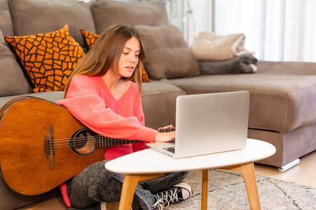 Mujer aprendiendo a tocar guitarra en casa con tutoriales en internet