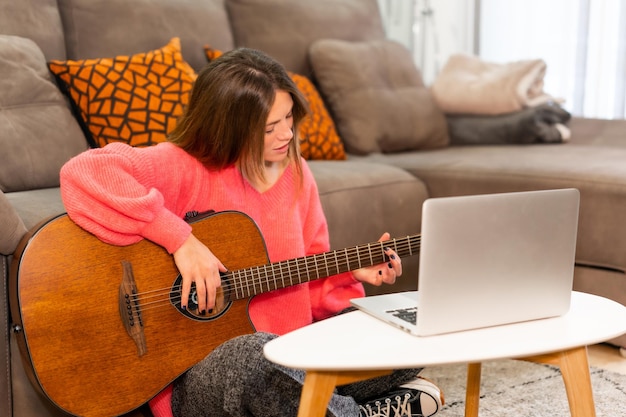 Mujer aprendiendo a tocar guitarra en casa con tutoriales en internet