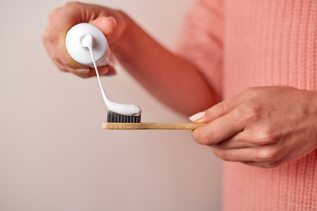 Mujer apretando pasta de dientes en el cepillo de dientes de bambú