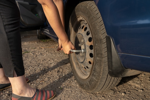 Mujer aprieta los tornillos de un disco mientras cambia el neumático manualmente en la rueda del coche