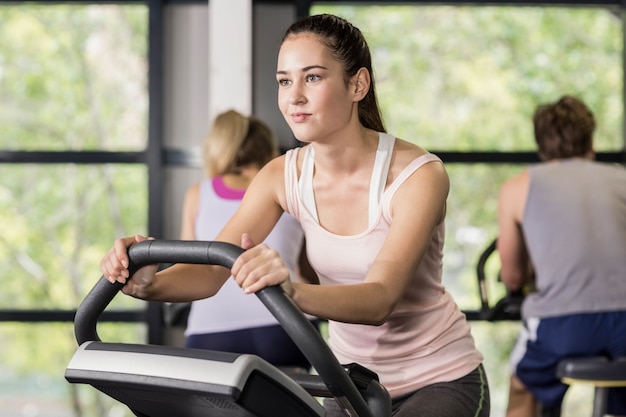 Mujer apta que hace bicicleta estática en el gimnasio