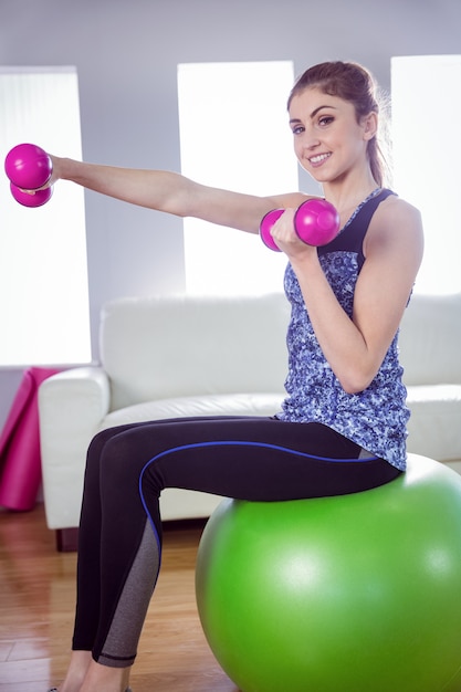 Mujer apta que levanta pesas de gimnasia en la bola del ejercicio