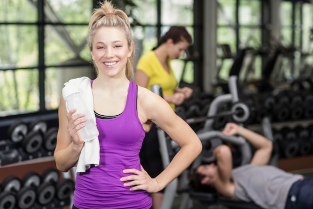 Mujer apta que presenta con la mujer y el hombre atléticos detrás en el gimnasio