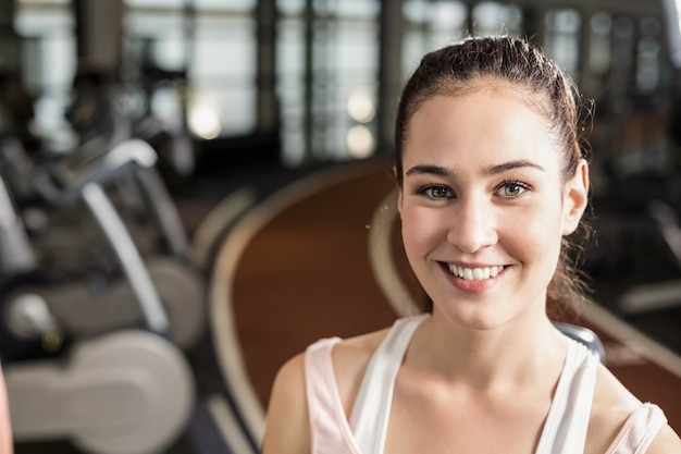 Mujer apta que sonríe a la cámara en el gimnasio