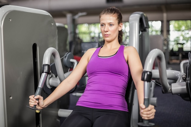 Mujer apta que usa la máquina de peso en el gimnasio