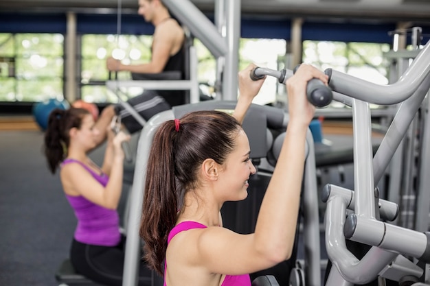 Mujer apta que usa la máquina de peso en el gimnasio