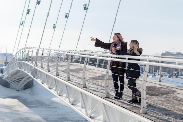 mujer apunta su mano a la distancia, de pie con un amigo en un puente peatonal en invierno