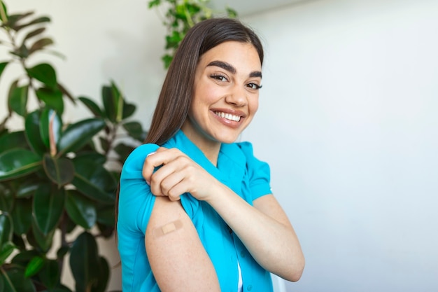 Foto mujer apuntando a su brazo con un vendaje después de recibir la vacuna covid-19. mujer joven mostrando su hombro después de recibir la vacuna contra el coronavirus