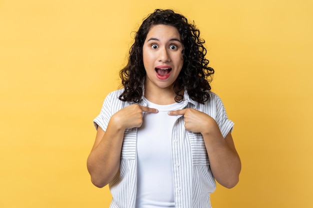 Foto mujer apuntándose a sí misma mirando con expresión sorprendida expresando un éxito increíble