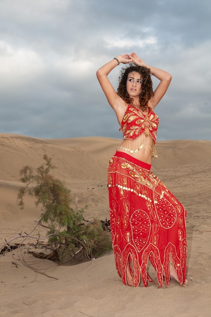 Mujer árabe bailando danza del vientre en las dunas del desierto al atardecer