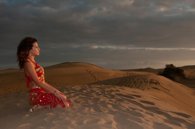 Mujer árabe bailando danza del vientre en las dunas del desierto al atardecer