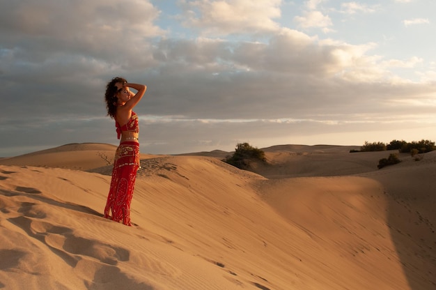 Mujer árabe bailando danza del vientre en las dunas del desierto al atardecer