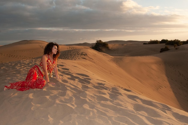 Mujer árabe bailando danza del vientre en las dunas del desierto al atardecer