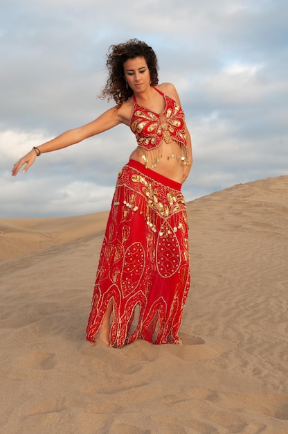 Mujer árabe bailando danza del vientre en las dunas del desierto al atardecer