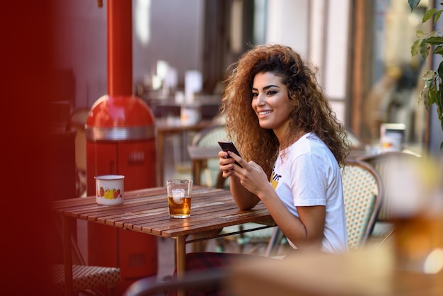 Mujer árabe en un bar urbano en su teléfono inteligente.