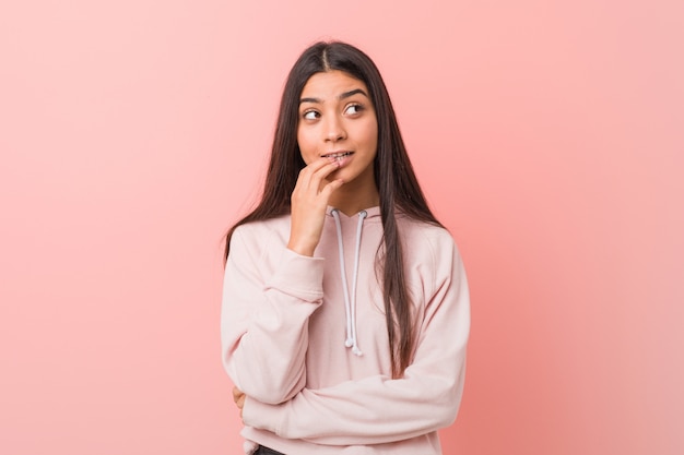 La mujer árabe bastante joven que lleva un deporte casual parece relajado pensando en algo que mira un espacio de la copia.