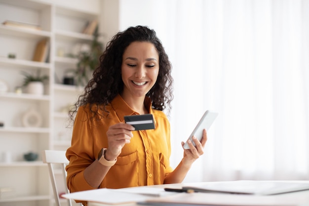 Mujer árabe feliz comprando en línea usando un teléfono celular en la oficina