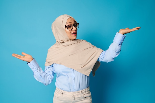 Mujer árabe en hijab posando con los brazos extendidos y las palmas hacia arriba, presentando