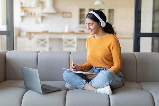 Mujer árabe india joven con auriculares estudiando en línea con una computadora portátil desde casa