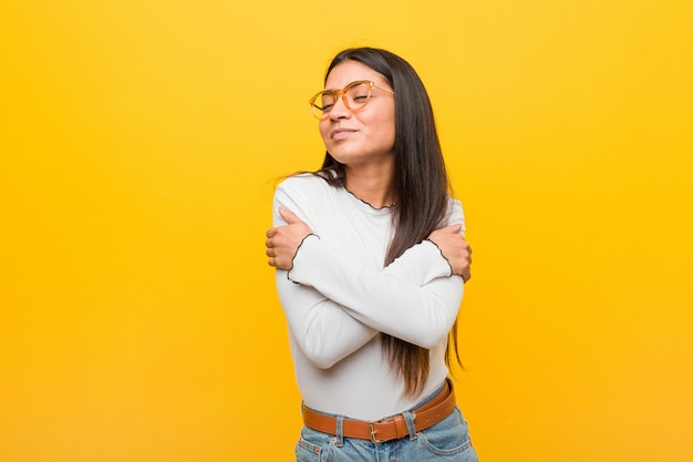 La mujer árabe joven bonita contra una pared amarilla abraza, sonriendo despreocupada y feliz.