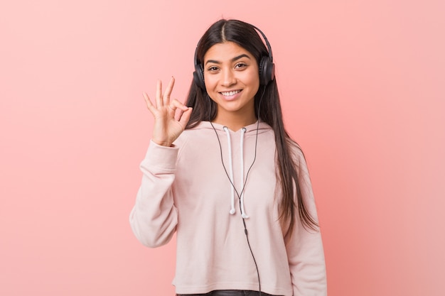 Mujer árabe joven que escucha la música alegre y confiada que muestra gesto aceptable.