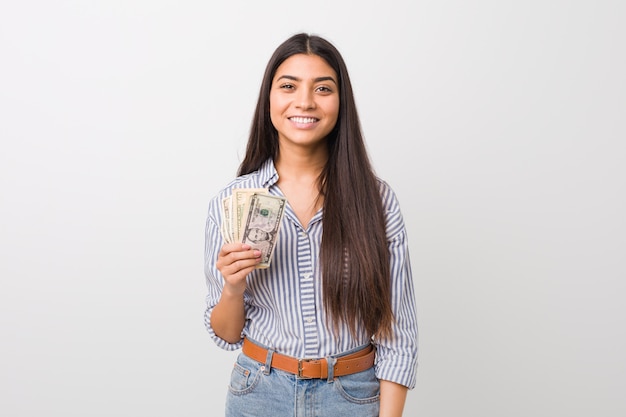 Mujer árabe joven que lleva a cabo dólares felices, sonrientes y alegres.